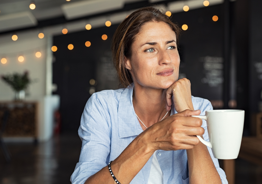Kvinna i blå skjorta som sitter med en kopp kaffe i handen