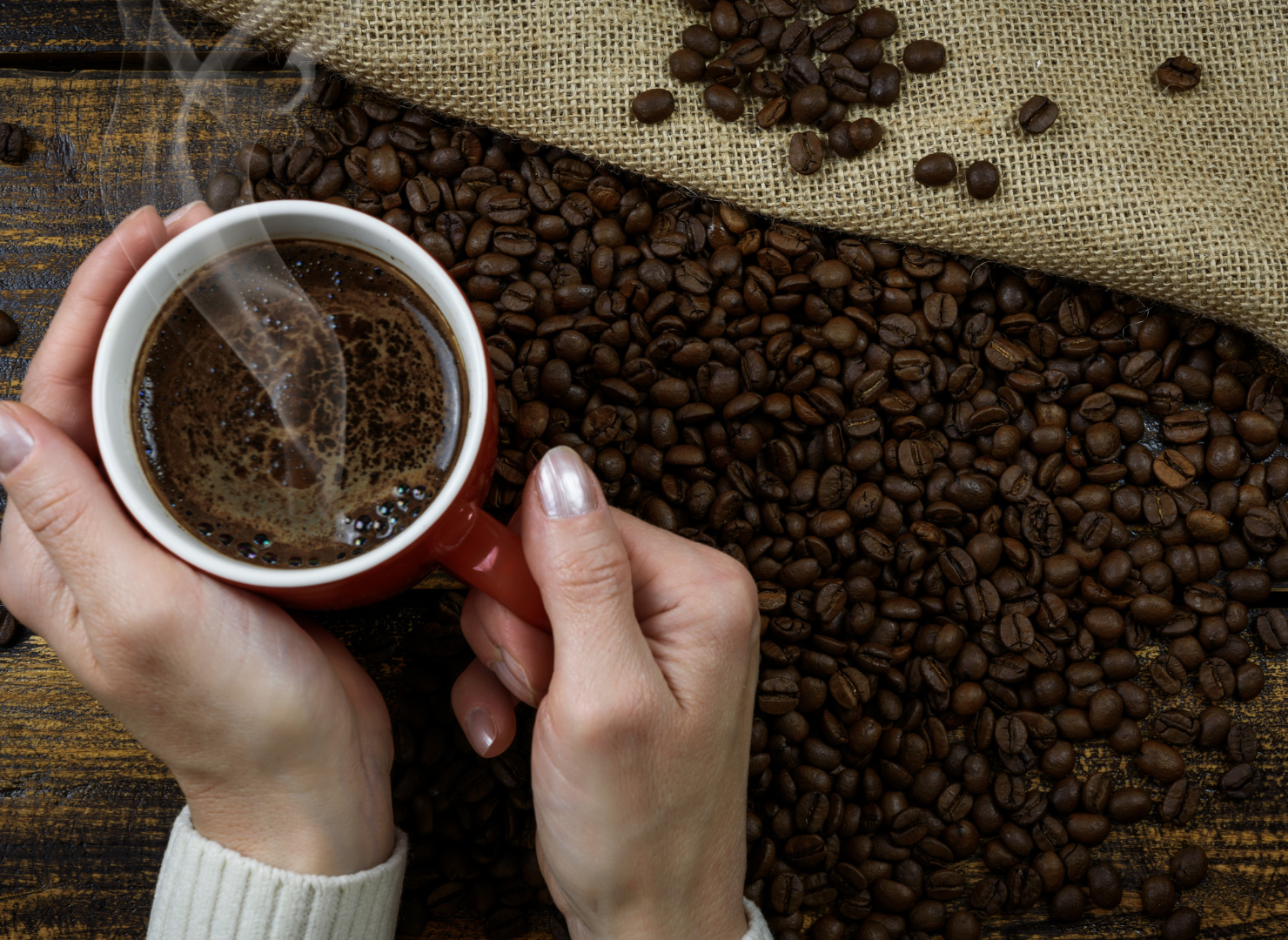 Kopp svart kaffe i röd mugg med bönor runt