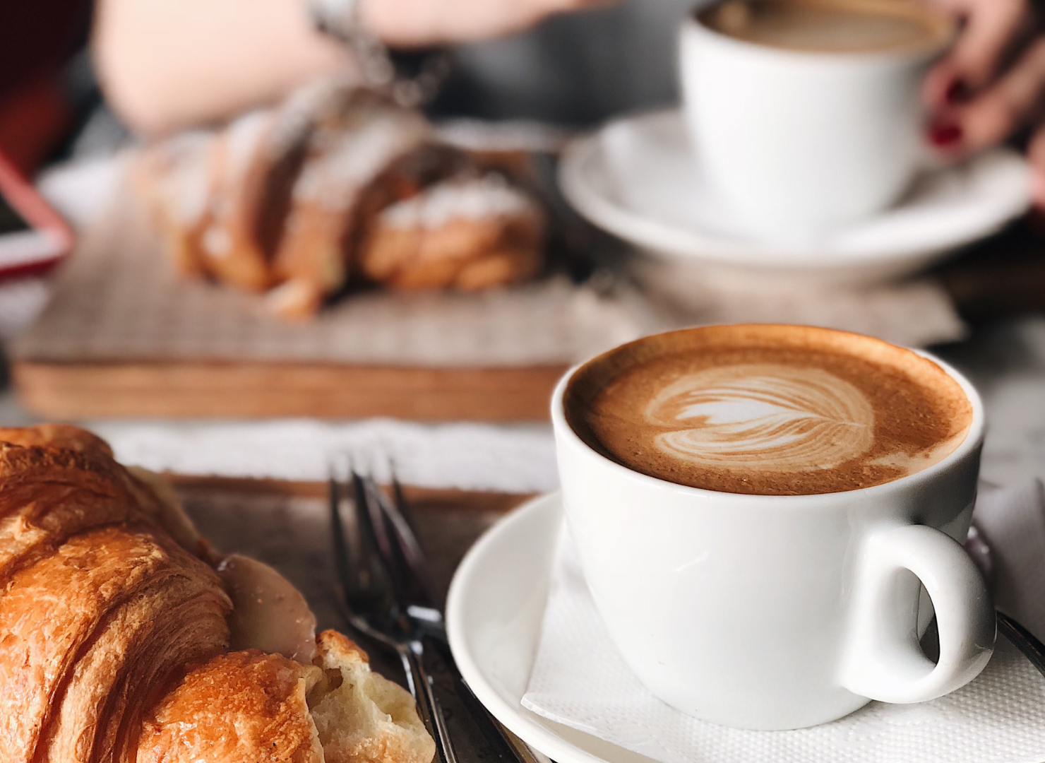 Kopp kaffe med mjölk bredvid en croissant