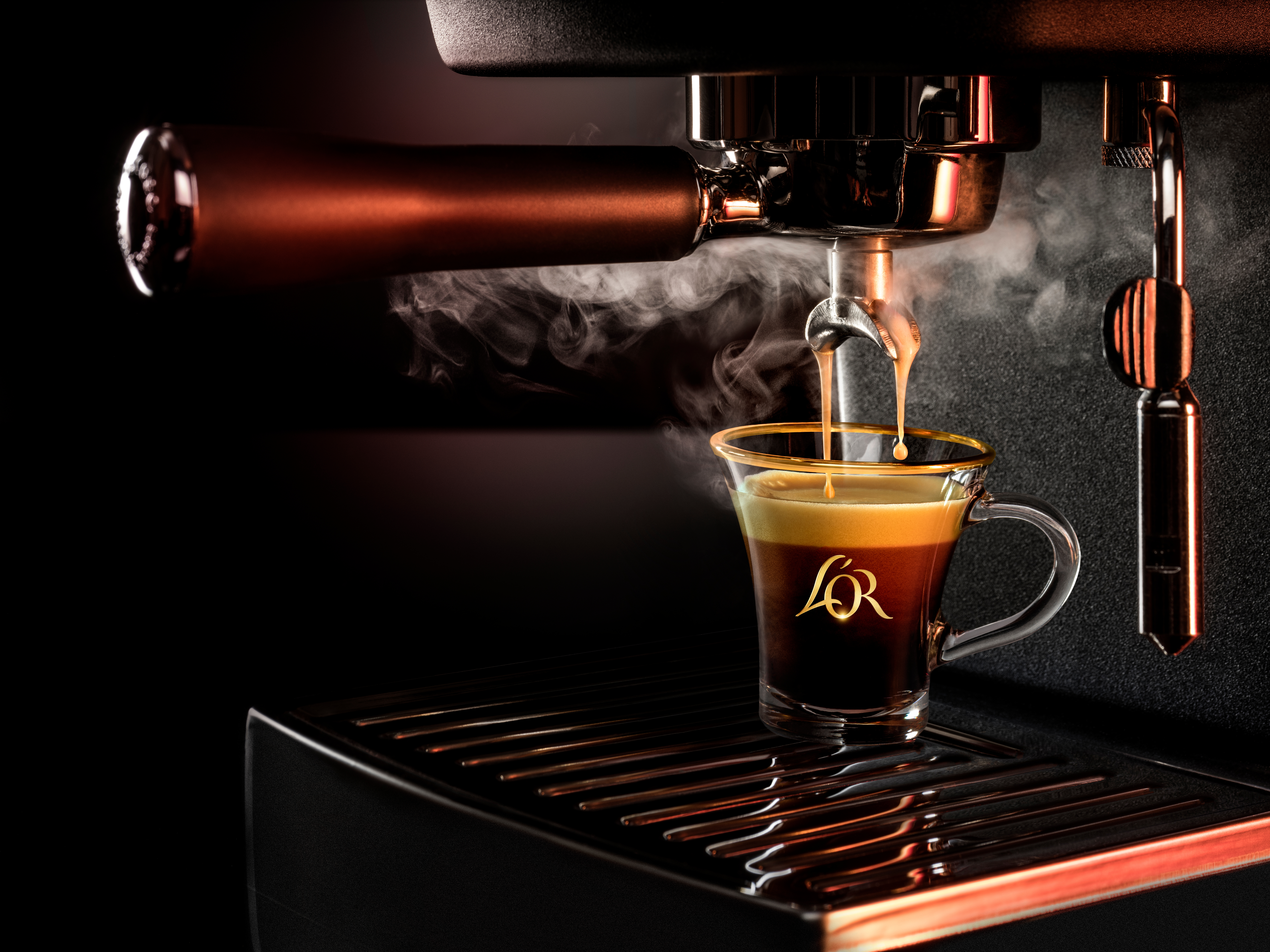 Närbild av en espressomaskin som brygger kaffe i en L'OR-glas kopp med synlig ånga.