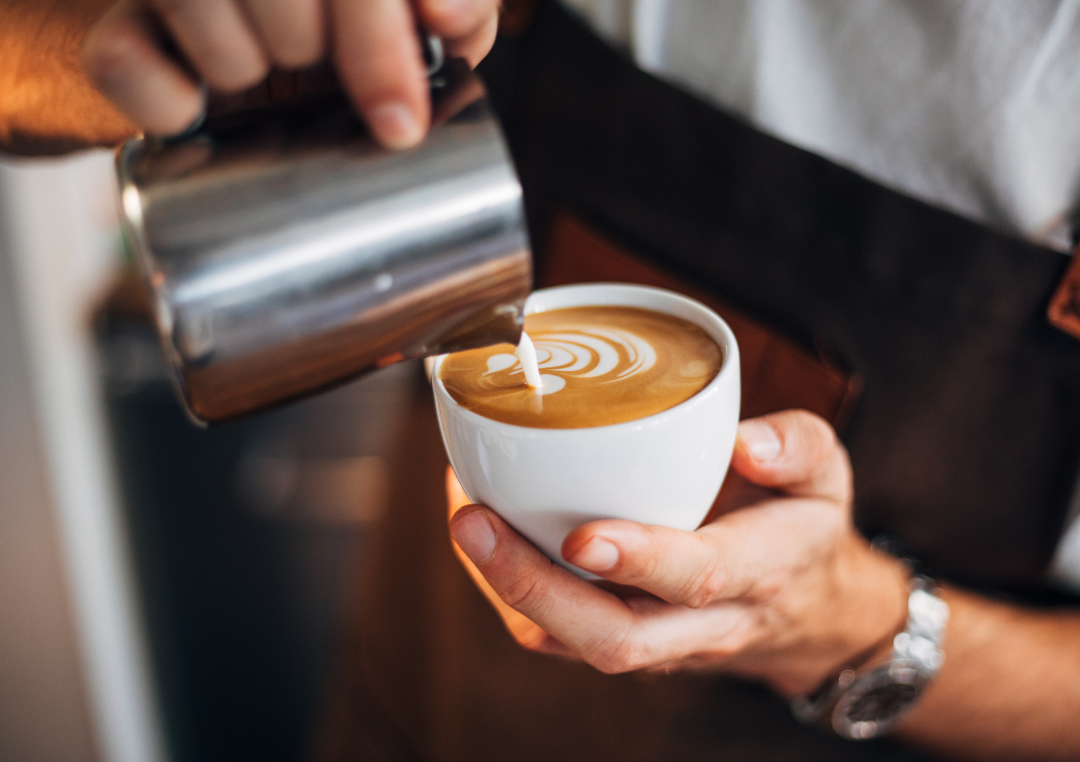 Man som häller mjölkskum i en kopp kaffe